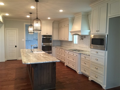 A modern kitchen with white cabinetry, a large central island with a marble countertop, and stainless steel appliances.