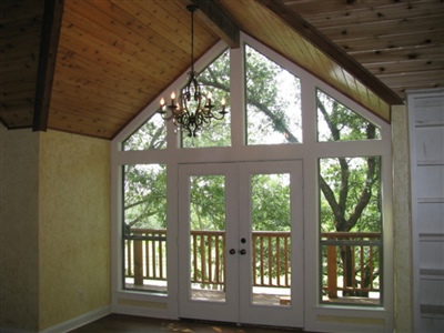 A room with high vaulted ceilings, large windows, and French doors leading to a balcony, illuminated by a chandelier.